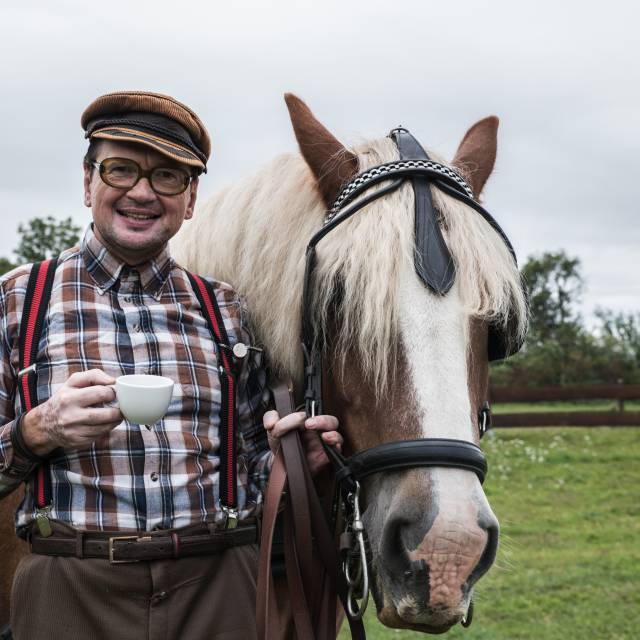 Herr steht neben Pferd mit einer Kaffeetasse