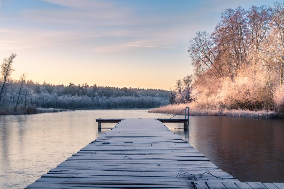 Gefrorener Steg am See in der Dämmerung im Winter